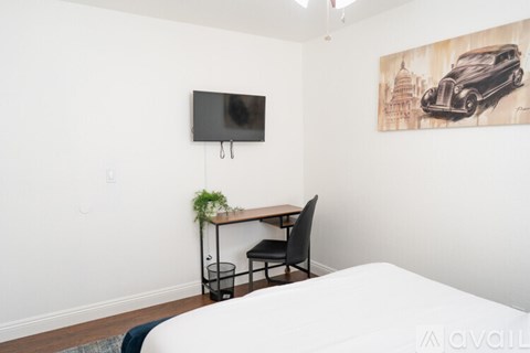 A room with a bed, desk, chair, and a painting of a car.