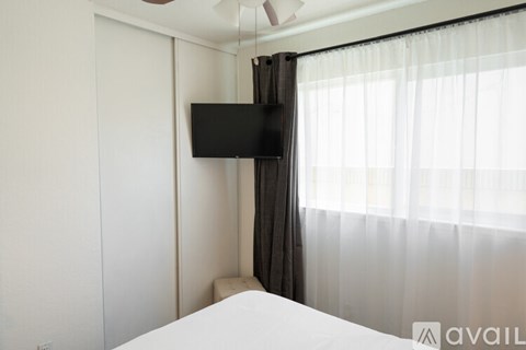 A bedroom with a bed, a television, and a window with curtains.