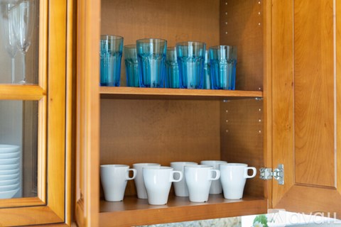 A wooden cabinet with glass doors is filled with blue glasses and white cups.