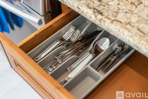 A drawer full of silverware is open and placed under a marble countertop.