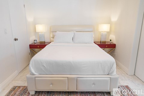 A bed with a white sheet and two pillows sits in a room with two lamps on either side of it.