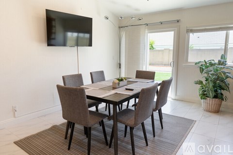 A dining room with a table and chairs and a flat screen TV mounted on the wall.