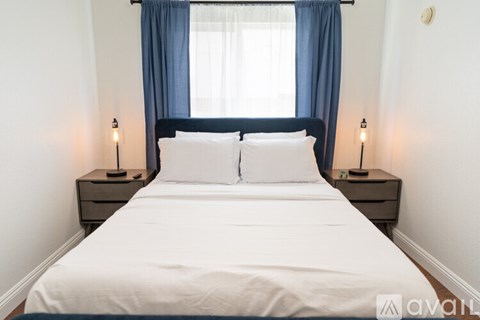 A bed with white sheets and two white pillows is flanked by two lamps on either side.