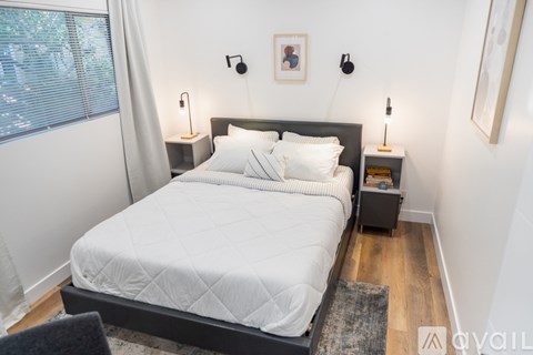 A bedroom with a large bed and a window with white curtains.