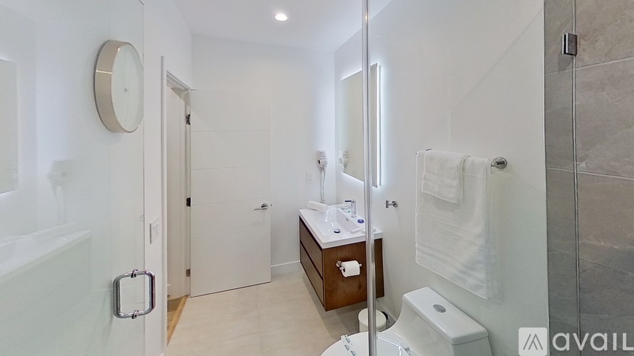 A bathroom with a toilet, sink, mirror, and a clock on the wall.