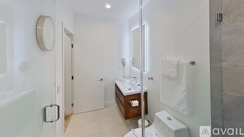 A bathroom with a toilet, sink, mirror, and a clock on the wall.