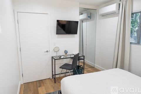 A bedroom with a bed, desk, chair, and a television mounted on the wall.