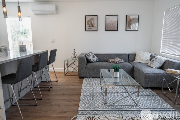 A modern living room with a grey couch, a glass coffee table, and a dining table with chairs.