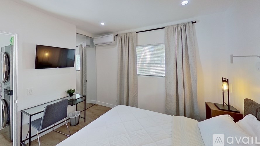 A bedroom with a large bed, a flat screen TV, and a glass table with chairs.