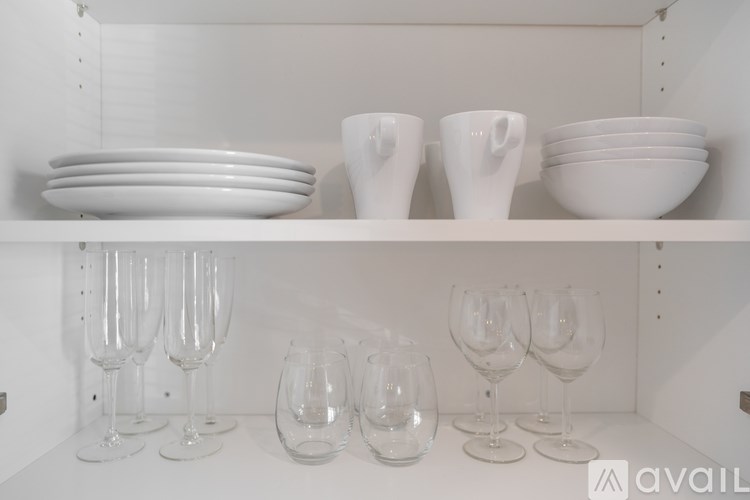 A white shelf with plates, cups and glasses on it.