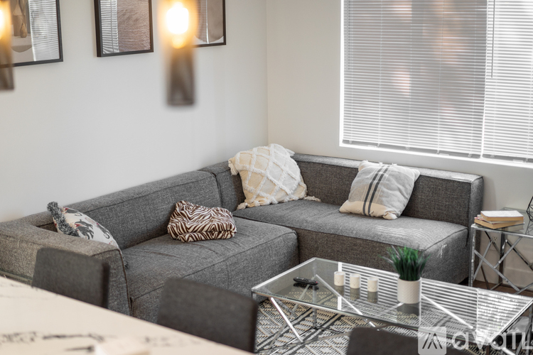 A grey couch with a glass coffee table in front of it.