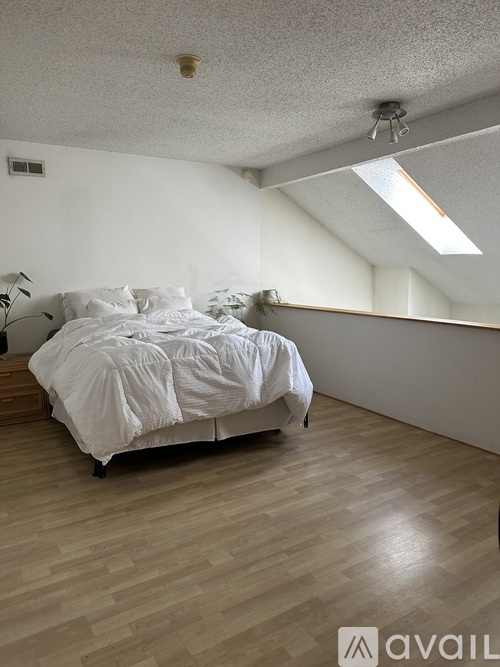 A bedroom with a bed, wooden floor, and a skylight.