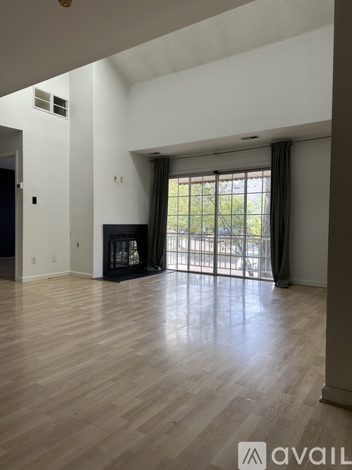 A spacious living room with wooden flooring and a large window with curtains.