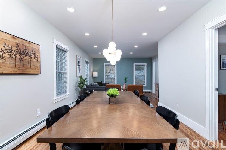 A long wooden table is surrounded by black chairs in a room with a large painting on the wall.