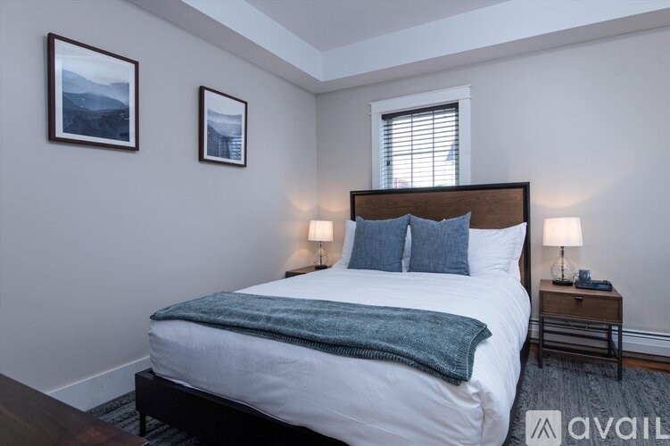 A bedroom with a bed, two lamps, and two pictures on the wall.