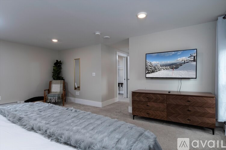 A bedroom with a large bed, a dresser, and a flat-screen TV mounted on the wall.