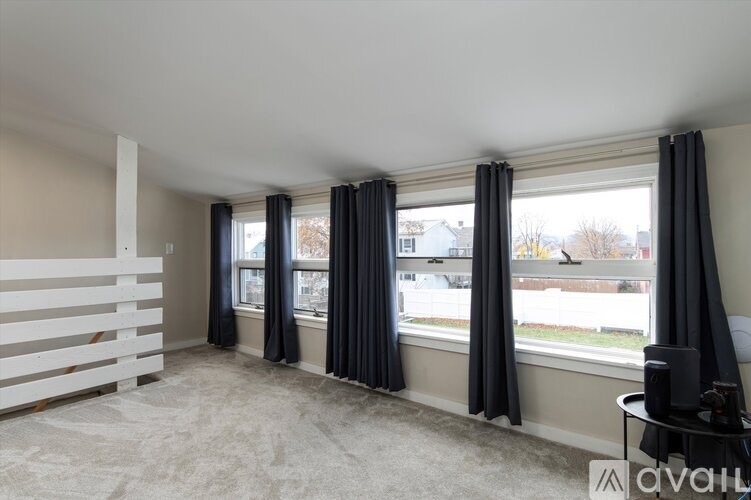 A room with a carpeted floor, a window with black curtains, and a white wall with a window sill.