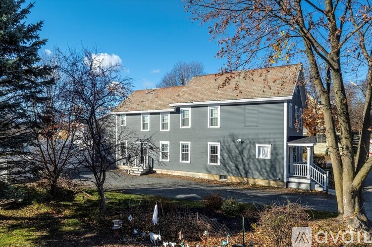 A grey house with a white fence and trees in the background.