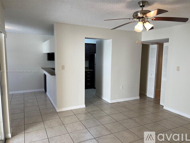 A spacious living room with a ceiling fan and a kitchen area in the background.