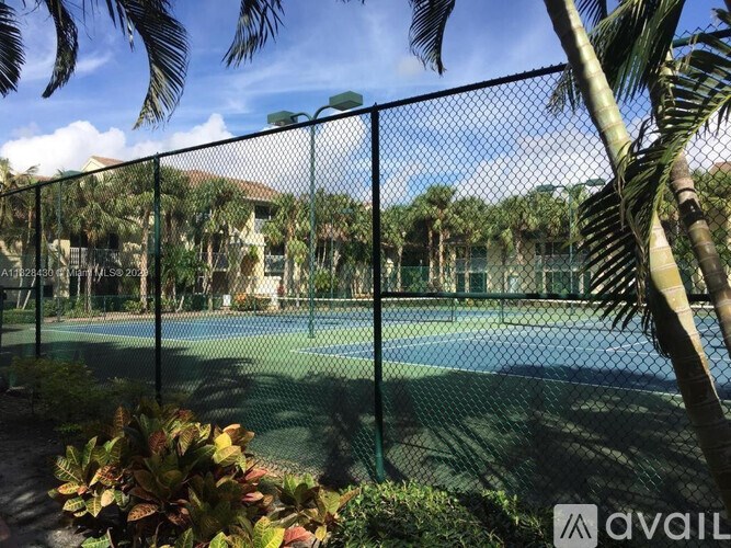 A tennis court surrounded by a fence and palm trees.
