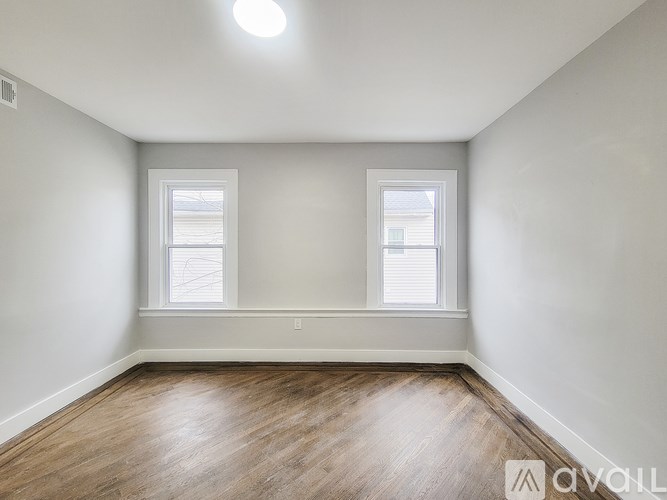 A room with wooden flooring and two windows.