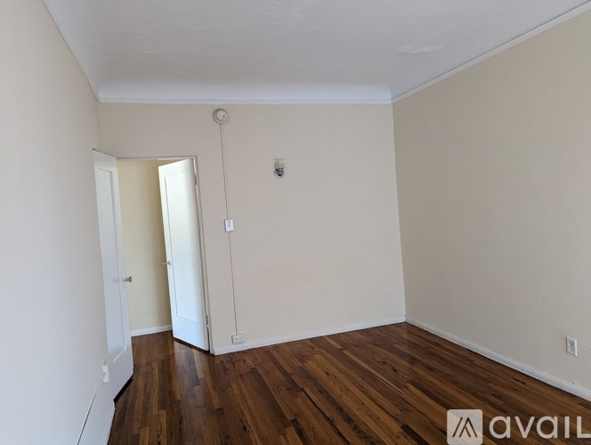 A room with wooden floors and white walls, with a doorway leading to another room.