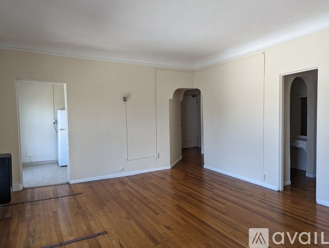 A room with wooden floors and white walls, with a door on the left and a window on the right.