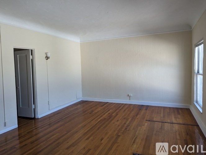 A room with wooden flooring and a door on the left side.