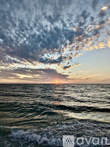 A sunset over the ocean with waves crashing in the foreground.