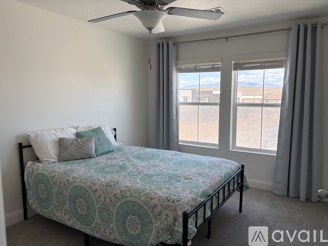 A bedroom with a bed, a ceiling fan, and a window with a view of the outdoors.