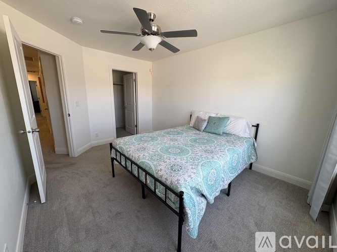 A bedroom with a bed, a ceiling fan, and a door leading to another room.