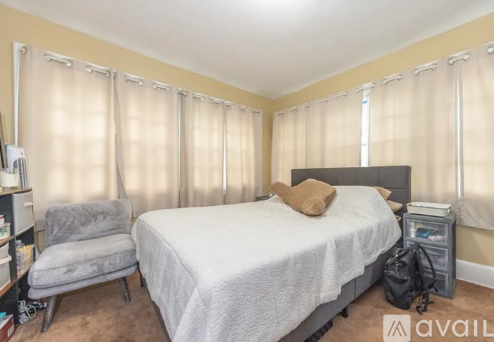 A bedroom with a bed, chair, and window with curtains.