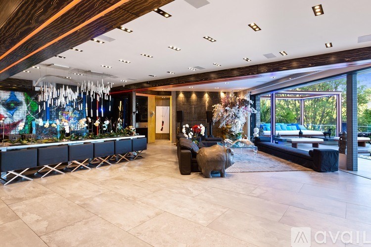 A spacious room with a long table and chairs, a large window with a view of trees, and a chandelier hanging from the ceiling.