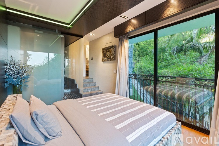 A bedroom with a large bed and a view of a balcony with greenery.