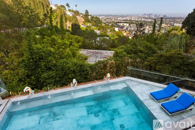 A swimming pool with two lounge chairs and a person sitting on one of the chairs.