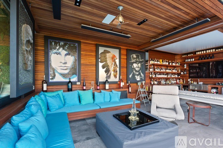 A blue couch is in the middle of a room with a wooden ceiling and a bar area.