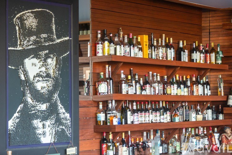 A bottle of liquor is on a shelf next to a picture of a man in a hat.