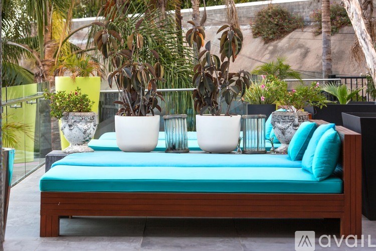 A wooden bench with a blue cushion and two white vases on it.