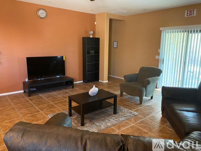 A living room with a brown leather couch, a black coffee table, a black television, and a black bookshelf.