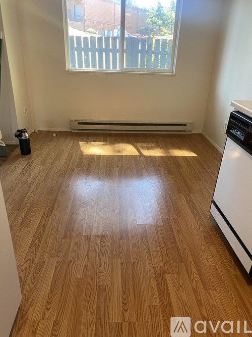 A room with wooden flooring and a window with a view of a fence.