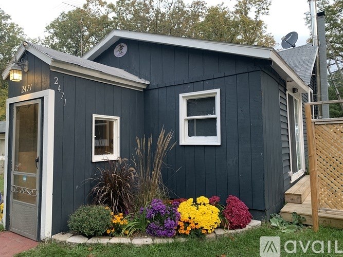 A blue house with a white window and a door is surrounded by flowers.