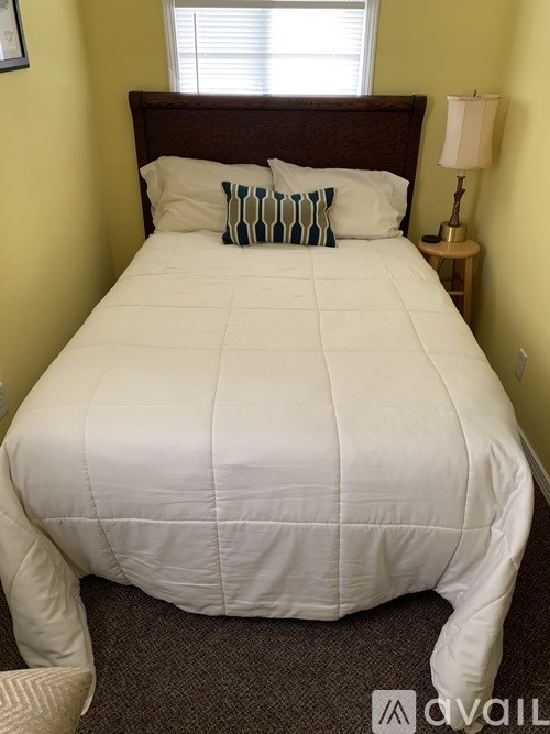 A bed with a white comforter and two pillows with green and blue stripes.