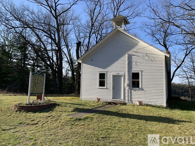 A small white church with a bell tower stands alone in a grassy field.