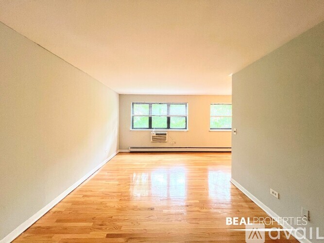 A spacious room with wooden floors and two windows.