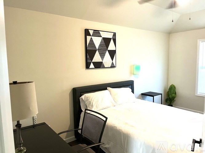 A bedroom with a bed, chair, lamp, and a picture on the wall.