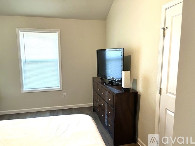 A bedroom with a bed, a window, and a television on a dresser.