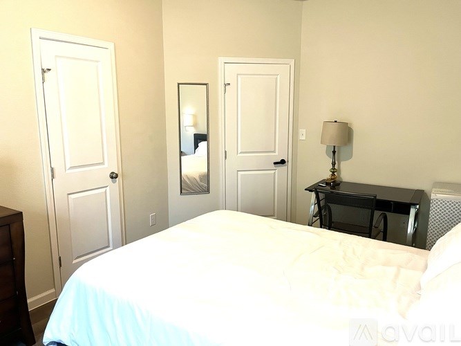 A bedroom with a bed, a desk with a lamp, and two doors.