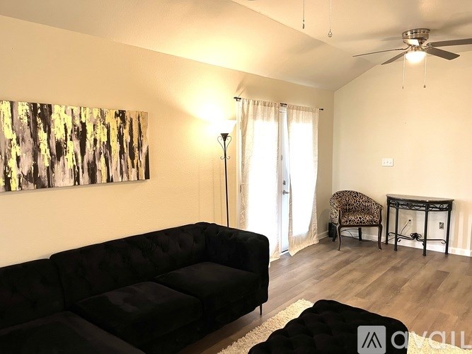 A living room with a black couch, a chair, and a painting on the wall.