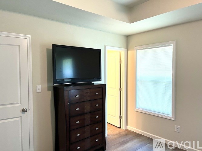 A black TV is mounted on a wooden cabinet in a room with a white door and a window with blinds.