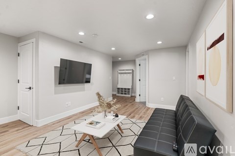 A living room with a black couch, a coffee table, and a television on the wall.